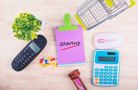 Starting new business concept,top view of notepad with word STARTUP, mobile phone, calculator, and other accessories on wooden backgroundの写真素材