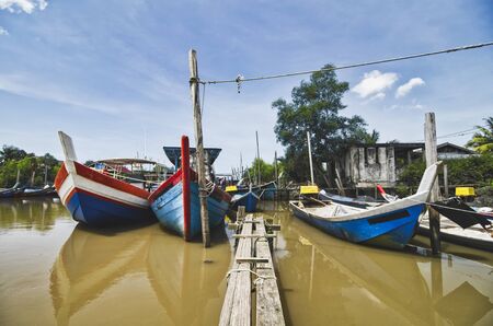 Beautiful rural scenery, fisherman boat moored near wooden jetty over blue sky backgroundの写真素材