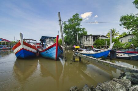 Beautiful rural scenery, fisherman boat moored near wooden jetty over blue sky backgroundの写真素材