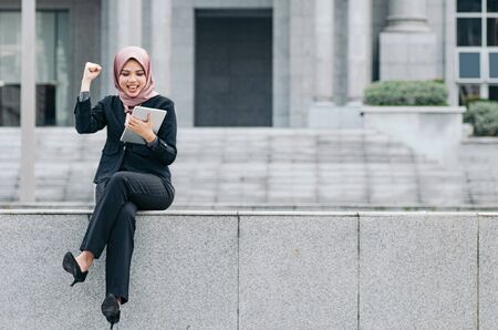 Portrait of cheerful happy businesswoman wearing black suit  sitting and holding tabletの写真素材