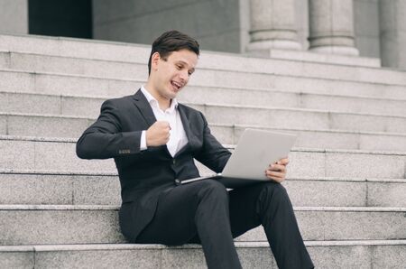 motivated expression young business man sitting on stairs  working with his laptop の写真素材