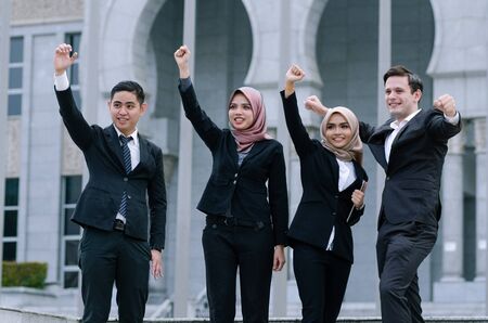 Group of young executive people in formalwear, arms raised to celebrate their successの写真素材