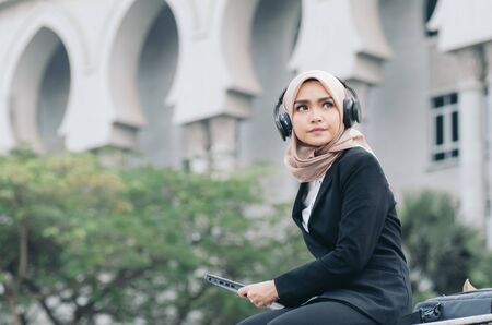 Portrait of beautiful woman in black suit and hijab smiling listening to music