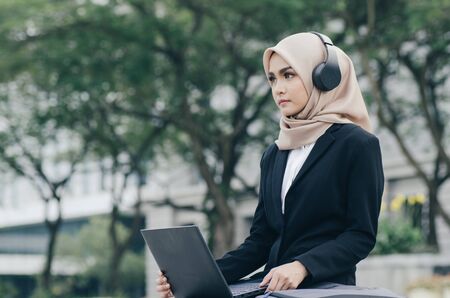 Portrait of beautiful woman in black suit and hijab smiling listening to music