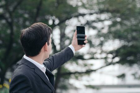 Portrait of young Businessman in black suit using a mobile phone for a video call with partners or...