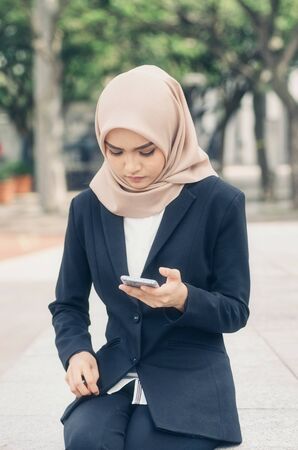 unhappy young business woman sitting and holding her mobile phoneの写真素材
