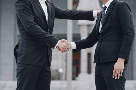 unidentified businessmen shaking hands together while standing infront their new modern officeの写真素材