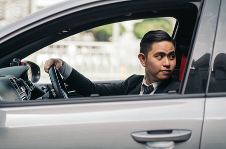smiling young businessman sitting in his car and look at the back