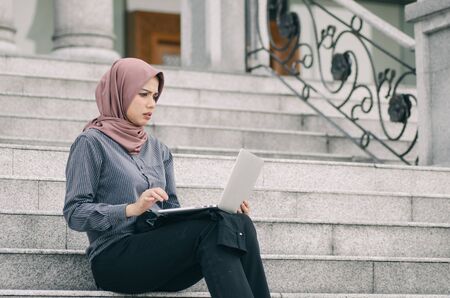 unhappy expression, young businesswoman sitting on stairs and  look at her laptopの写真素材
