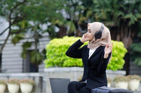 Portrait of beautiful woman in black suit and hijab smiling listening to musicの写真素材