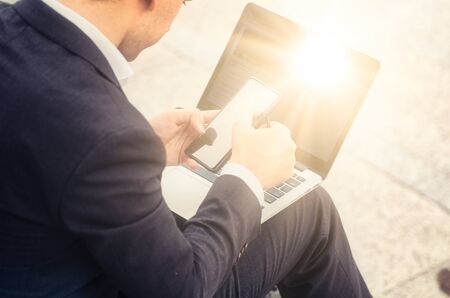 unidentified young businessman in elegant suit with laptop,sitting and using his mobile phoneの写真素材