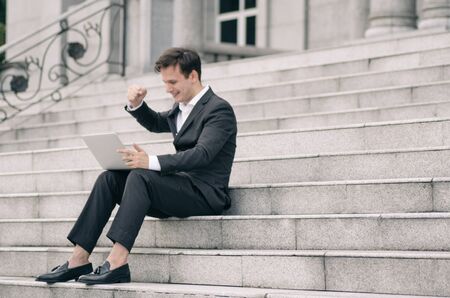 smile face young business man sitting on stairs and working with his laptop.selective focus shotの写真素材