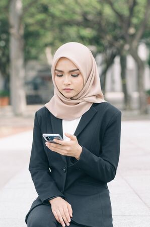 unhappy young business woman sitting and look at her mobile phoneの写真素材