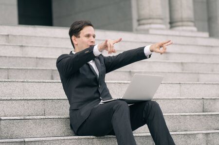 smiling and happy young business man sitting on stairs  working with his laptopの写真素材
