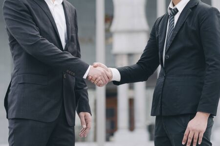 unidentified businessmen shaking hands together while standing infront their new modern officeの写真素材