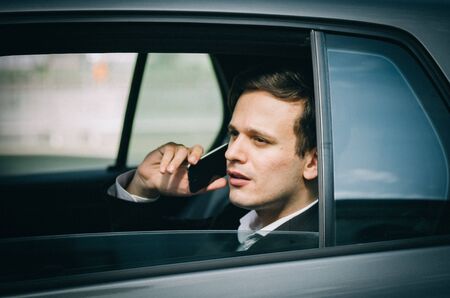 Confident and successful expression, young businessman talking on the mobile phone and leaning on the window.の写真素材