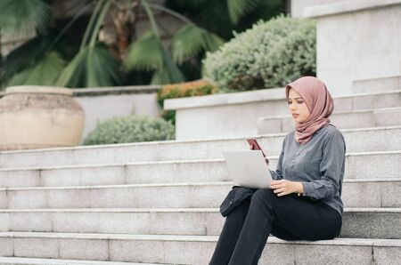 Beautiful asian businesswoman with laptop relaxing on stairs, and typing SMS.copyspace on left for textの写真素材