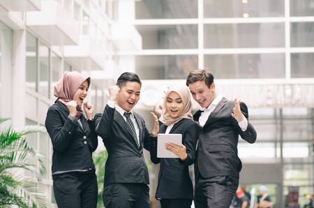 Happy successful young business people look at tablet and cheer their successの写真素材