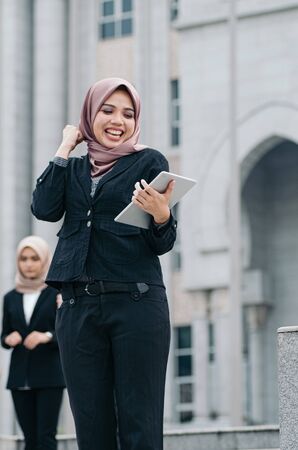 Portrait of cheerful happy businesswoman wearing black suit  standing  and holding tablet の写真素材