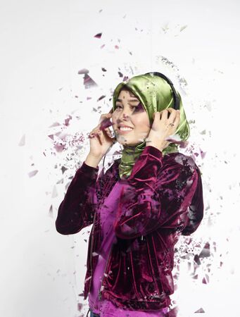 Studio shot, portrait of young beautiful Asian muslim wearing hijab listening to music with headsetの写真素材