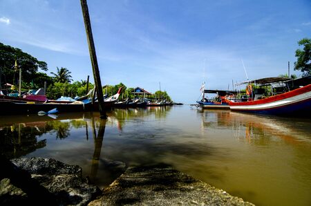 Beautiful rural scenery, fisherman boat moored near wooden jetty over blue sky backgroundの写真素材