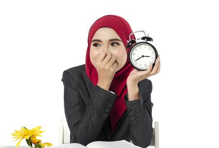 Smiling asian business woman with hijab holding alarm clock against white backgroundの写真素材