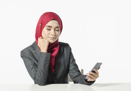 Communication concept, young woman with hijab sitting with eye closed, holding her handphone against white backgroundの写真素材