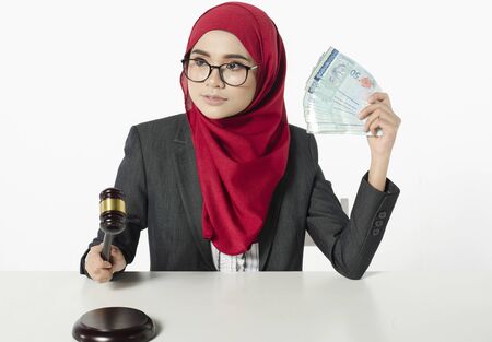 Auction bidding or judicial system corruption concept,portrait of young woman in hijab holding money and judge gavel.の写真素材
