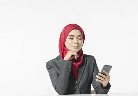 Communication concept, young woman with hijab sitting and texting her friends using her handphone against white backgroundの写真素材