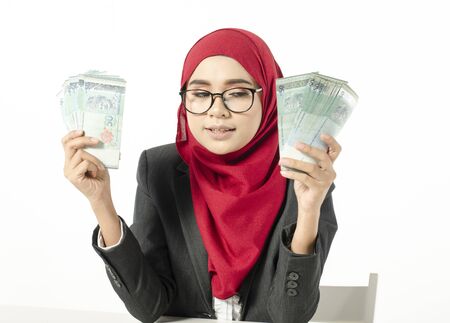 Portrait of satisfied young businesswoman in hijab looks with desire on moneyの写真素材