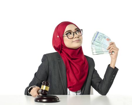 Auction bidding or judicial system corruption concept,portrait of young woman in hijab holding money and judge gavel.の写真素材