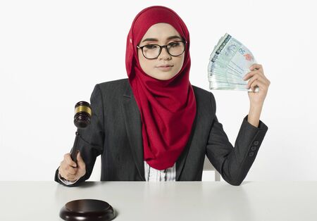 Portrait of satisfied young businesswoman in hijab looks with desire on moneyの写真素材