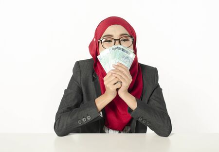 Portrait of satisfied young businesswoman in hijab, holds in her hands a lot of moneyの写真素材