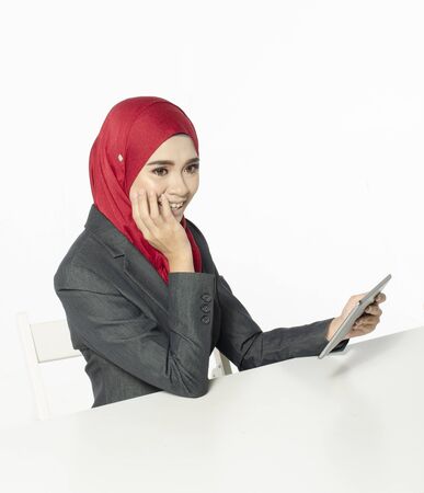 Communication concept, young woman with hijab sitting with smile face, look at her tablet against white backgroundの写真素材