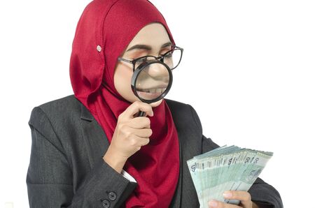 young woman in hijab looking on money through magnifying glass for authenticity checkingの写真素材