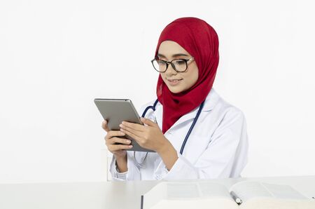 Smile face young doctor with hijab read her tablet pc in her office over white backgroundの写真素材