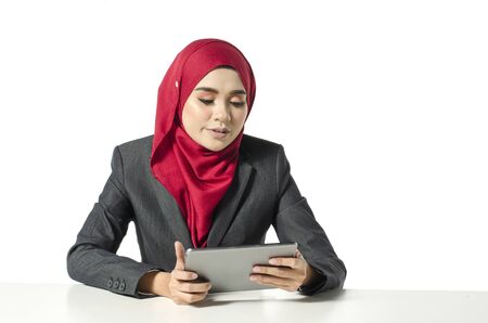 Communication concept, young woman with hijab sitting with smile face, look at her tablet against white backgroundの写真素材