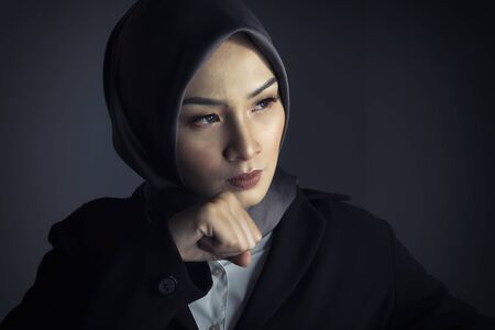 young confident bsinesswoman with hijab in suit standing over dark backgroundの写真素材