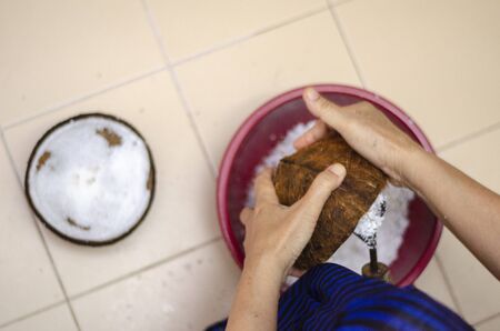 Traditional way, housewife sit on wooden coconut grater and grate coconut into containerの写真素材