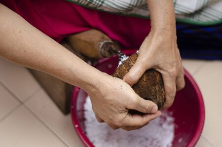 Traditional way, housewife sit on wooden coconut grater and grate coconut into containerの写真素材