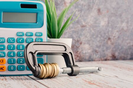 financial crisis concept, calculator and stacking coin squeezing in a G-clamp on wooden desk の写真素材