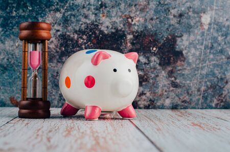 saving money for future concept, piggy bank and hourglass on wooden desk