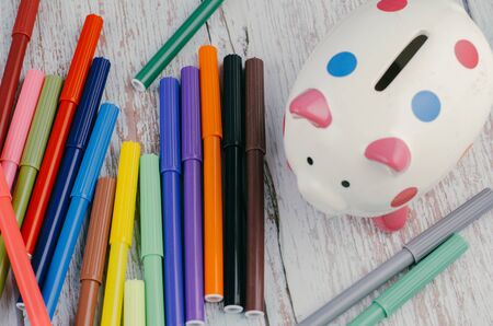 saving for education or back to school concept, piggy bank and colorful marker pen on wooden desk.の写真素材