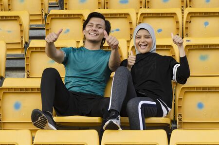 young couple sit in stadium with happy face expression, having fun and cheering to their teamの写真素材