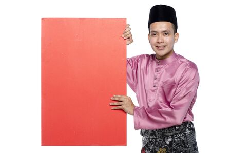 Portrait of young muslim with malaysian traditional attire called baju melayu standing  and holding card against white backgroundの写真素材