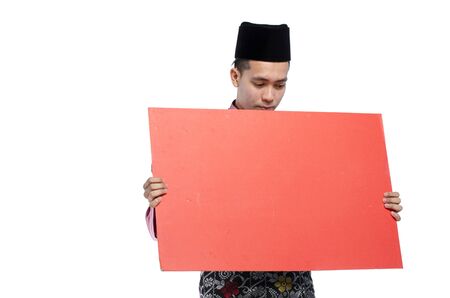 Portrait of young muslim with malaysian traditional attire called baju melayu standing  and holding card against white backgroundの写真素材