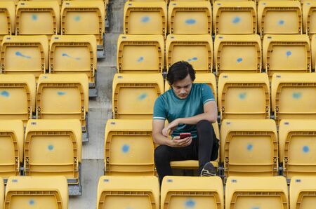 young man holding handphone sit in stadium with unhappy expression