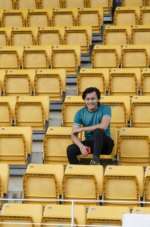 young man holding handphone sit in stadium with happy face expressionの写真素材