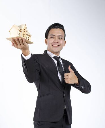 Portrait of young real estate agent in black suit holding home replica against white backgroundの写真素材