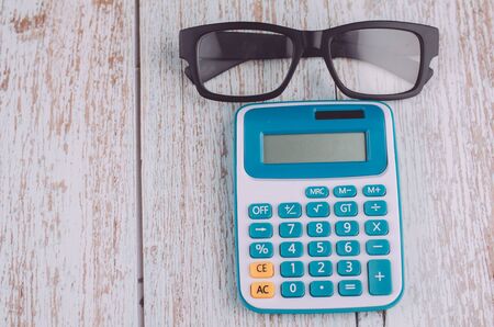 white calculator and eye glass on wooden desk for business and copy spaceの写真素材